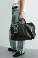 Bolso de viaje de diseño rectangular con acabado craquelado en tono oscuro. Cuenta con doble asa de mano, compartimento principal con cierre de cremallera, bolsillo interior con cierre y correa de hombro ajustable y extraíble.