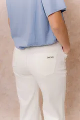 Pantalón jean de tiro alto y corte wide leg, color off white. Presenta un diseño minimalista con bolsillos funcionales, cierre frontal con botón y detalles metálicos plateados.