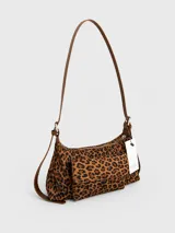 Cartera tipo baguette con estampado animal print, confeccionada en material suave símil gamuza. Presenta un bolsillo frontal con solapa y cierre, compartimento principal con cierre superior, y asa larga regulable de cuero sintético marrón.