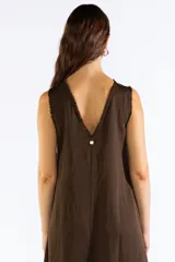 Vestido largo sin mangas color marrón, de corte amplio y fluido con escote bote. Cuenta con bolsillos laterales y detalles de terminaciones deshilachadas.