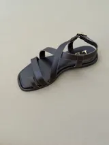 Sandalias de cuero color marrón con diseño de tiras cruzadas en el empeine, sujetador para el dedo y tira ajustable con hebilla en el talón.