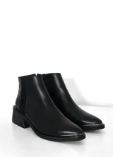 Bota corta de cuero negro con diseño tipo chelsea, presenta un panel elástico lateral y un taco cuadrado robusto. Incluye un detalle metálico en la puntera.