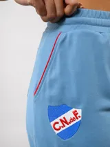Pantalón de piqué recto color azul marino, con cintura elástica y cordón ajustable. Presenta el escudo del Club Nacional de Football en el muslo izquierdo y el logo de Umbro en el muslo derecho.