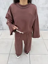 Buzo oversize de color marrón chocolate, con cuello redondo, mangas anchas y diseño con costuras expuestas en contraste. Presenta terminaciones desflecadas en el ruedo y en los puños.