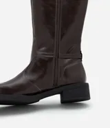 Bota de montar de caña alta confeccionada en poliuretano, con suela robusta, punta redondeada y detalle de hebilla metálica lateral. Cuenta con cierre lateral para mayor practicidad.