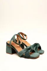 Sandalia de tacón cuadrado medio, confeccionada en terciopelo negro. Presenta un diseño de tiras cruzadas con nudo en la parte delantera y una tira ajustable con hebilla en el tobillo.