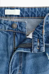 Jean de tiro alto con corte wide leg y diseño de cinco bolsillos. Presenta un acabado en denim azul con detalles de roturas desgastadas en la parte frontal.