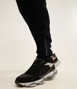 Pantalón deportivo de corte ajustado, confeccionado en tejido de poliéster texturizado color negro. Presenta cintura elástica con cordón de ajuste, bolsillos laterales con cierre y puños elásticos en los tobillos.