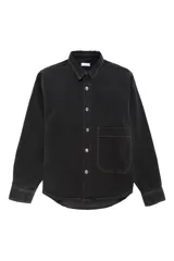 Sobrecamisa de denim en color negro lavado, con cierre frontal de botones metálicos, cuello clásico y un bolsillo de parche en el pecho. Presenta costuras a la vista y puños abotonados.