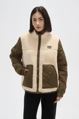 Campera de diseño híbrido que combina paneles de corderito sintético en color crema con mangas y bolsillos de tela técnica acolchada en color verde militar. Presenta cierre frontal completo, cuello alto y un pequeño parche decorativo en el pecho.