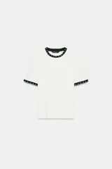 Camiseta blanca de manga corta y cuello redondo, con ribete negro decorado con perlas blancas en el cuello y los puños.