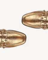 Mocasines dorados con punta fina y apliques de tachas doradas.