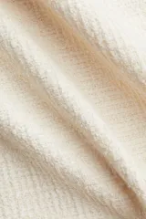 Pollera mini de tejido bouclé color crema, de tiro alto con elástico oculto en la cintura y bajo desflecado.