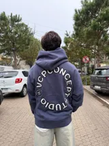 Buzo canguro oversize de algodón, color azul oscuro, con capucha y diseño gráfico circular estampado en la espalda con la inscripción VCP CONCEPTS STUDIO.