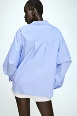 Camisa de manga larga en tejido de popelín color celeste, con cuello solapa, cierre frontal con botones y detalle de pliegue en el bajo.