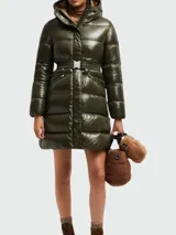 Campera larga tipo puffer de Moncler, color verde oliva con acabado brillante. Presenta capucha integrada, cierre frontal con cremallera y cinto ajustable en la cintura con hebilla metálica.