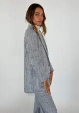 Blazer de lino y algodón en tono beige con textura a rayas verticales sutiles. Presenta solapas clásicas, un solo botón frontal marrón y un corte ligeramente holgado. Los bordes de las mangas y el ruedo tienen un acabado deshilachado.