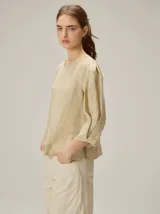 Blusa de algodón color marrón, con escote redondo, mangas tres cuartos con volumen sutil y costuras verticales decorativas en el frente.