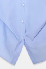 Camisa de popelín color celeste claro, con cuello solapa, manga larga y detalle de pliegue asimétrico en el bajo frontal.