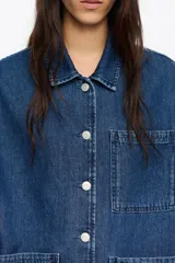 Chaqueta de denim azul de corte recto y holgado, con cuello camisero, cierre frontal de botones y cuatro bolsillos de parche (dos en el pecho y dos en el bajo).