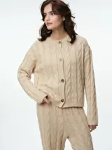Cárdigan de punto con diseño de ochos, color beige, con cuello redondo, cierre frontal de botones tipo carey y puños acanalados.