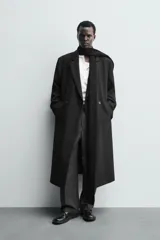 Abrigo largo de corte relajado en color negro, confeccionado en tejido con viscosa. Presenta un diseño de botonadura cruzada, cuello con solapas de pico, manga larga con puños abotonados y bolsillos laterales de vivo. Incluye una abertura en el centro de la espalda y un bolsillo interior.