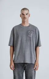 Remera de corte oversize color gris melange, con cuello redondo y mangas cortas. Presenta un estampado en la espalda inspirado en la carta del tarot 'El Mundo', con diseño gráfico detallado y tipografía alusiva.