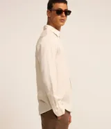 Camisa de manga larga color crema, con cuello inglés, abotonada y textura de rayas verticales.