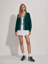 Cárdigan de punto verde oscuro con cuello en V y botones. Presenta ribetes blancos en el cuello, el frente y los puños.