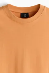Remera de algodón de peso medio, color naranja, con cuello redondo ribeteado y hombros caídos de corte relajado.