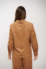 Camisa de manga larga color tostado, con cuello clásico y cierre frontal de botones. Presenta un diseño de corte recto y acabado suave.