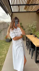 Vestido largo de jean color blanco, con cuello camisero, mangas cortas, cierre frontal con botones y tajo lateral.