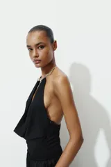 Body negro de cuello halter con detalle de pieza metálica y aplicación joya. Escote pico pronunciado y tejido drapeado. Cierre en bajo con botones a presión.