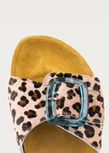 Sandalia plana con plantilla ergonómica y suela de corcho. Capellada de cuero con estampado animal print tipo leopardo y tira ancha ajustable con hebilla grande de resina translúcida en tono azulado.
