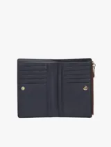 Billetera bifold Tommy Hilfiger de color bordó, confeccionada en poliuretano con acabado texturizado. Presenta un cierre principal con cremallera y un detalle frontal con logo metálico distintivo de la marca y broche.