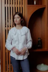 Camisa blanca de lino con cuello babero de broderie y mangas largas.
