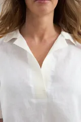 Blusa blanca de lino con silueta cómoda y relajada, escote en V con cuello polo y detalles en algodón.