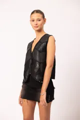 Chaleco negro de cuero artesanal con diseño de paneles combinados en cuero liso y cuero grabado con motivos florales. Presenta terminaciones en crochet, apliques calados en el bajo y cierre frontal con dije de borla.