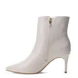 Botas de caña baja marca Bottero, color marfil, con punta fina y taco aguja. Presentan un diseño minimalista con cierre lateral y detalle de placa metálica con logo en la parte superior.