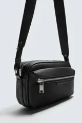 Bandolera negra con textura grabada, compartimento principal con cierre de cremallera, bolsillo interior con cremallera, bolsillo frontal con cremallera y asa de hombro ajustable.