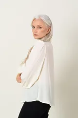 Blusa color marfil de manga larga con frunce en hombros y puños, escote en V con lazo y cierre de puños con dos botones.