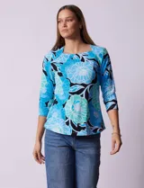 Remera de algodón estampada con flores en tonos celeste, azul y verde, sobre fondo negro. Tiene mangas 3/4 y escote cuadrado.