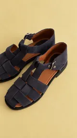 Sandalias cangrejeras de gamuza color azul marino, con punta redonda, tiras entrelazadas, talonera cerrada y hebilla de metal ajustable en el lateral.