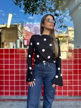 Blusa negra con estampado de lunares blancos, de corte ajustado al cuerpo, cuello redondo y mangas largas con terminación acampanada.