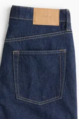 Pantalón jean de tiro alto y cinco bolsillos, confeccionado en denim de algodón rígido en color azul oscuro, con perneras amplias y corte holgado.