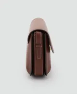 Bolso de hombro tipo bandolera en color marrón, con diseño estructurado de solapa, cierre metálico a presión y costuras decorativas en contraste. Incluye correa larga ajustable.