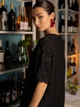 Vestido corto de tejido de punto con destellos de lurex, color bordó. Presenta un diseño holgado con mangas cortas, cuello redondo y terminaciones onduladas en los bordes.