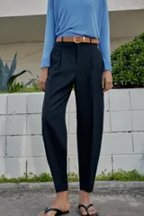 Pantalón tobillero azul marino de tiro medio, con pinzas delanteras, bolsillos frontales, falsos bolsillos con solapa en la espalda y cierre frontal con cremallera, botón y gancho. Incluye cinturón de cuero sintético tostado con hebilla metálica dorada.