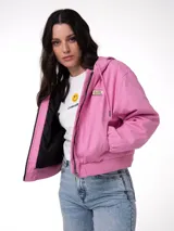 Chaqueta de lona color rosado con capucha ajustable, cierre frontal de cremallera, bolsillos laterales y forro interior acolchado negro. Cuenta con parche del logo de la marca en el pecho.