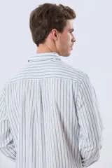Camisa de manga larga de lino y algodón, con diseño de rayas verticales en tonos celestes y blancos. Presenta cuello camisero, cierre frontal con botones y pequeño bordado al tono en el pecho.